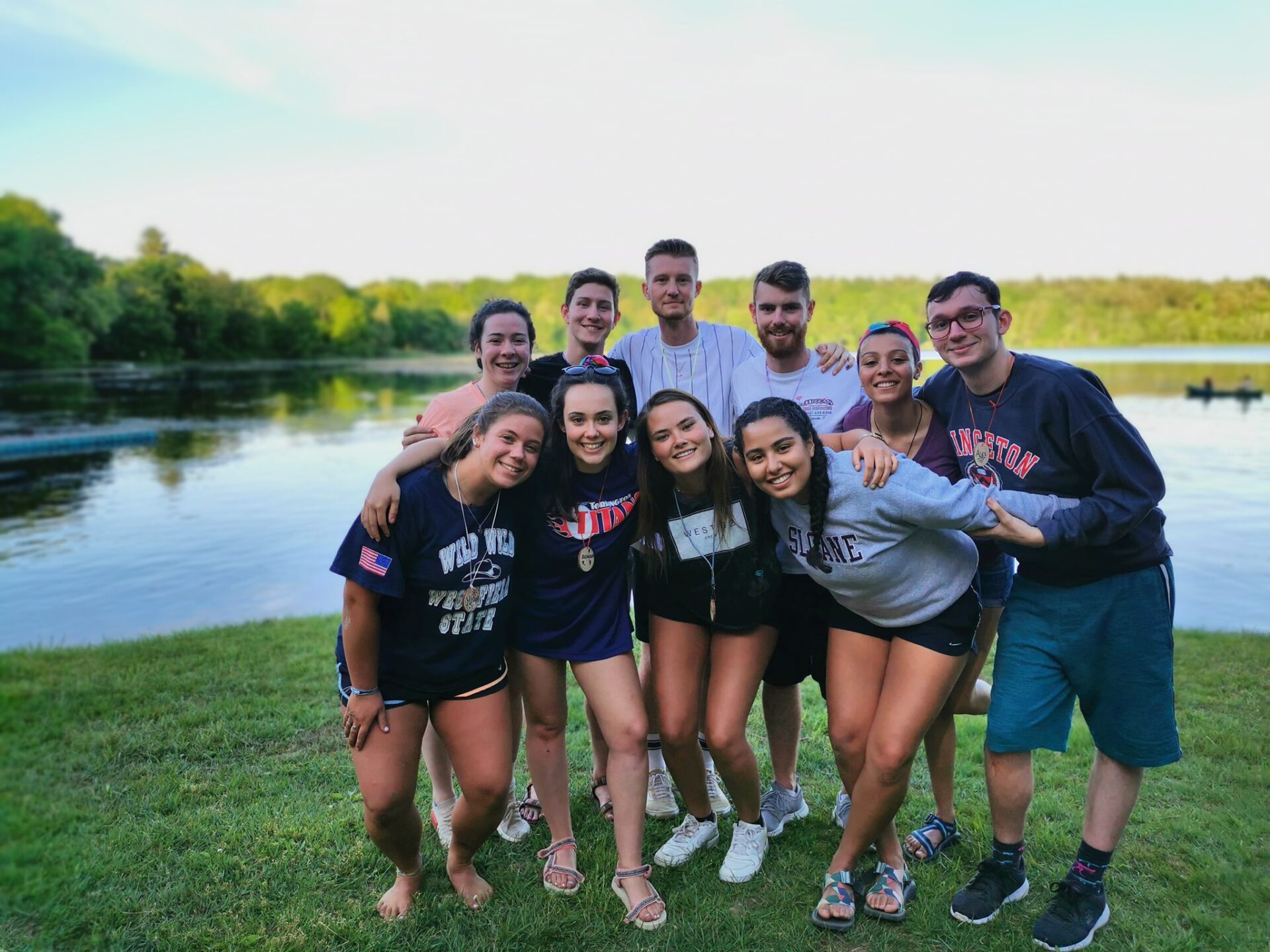 Camp Connect USA - Group of people posing outdoors by a lake, smiling and wearing casual clothes.