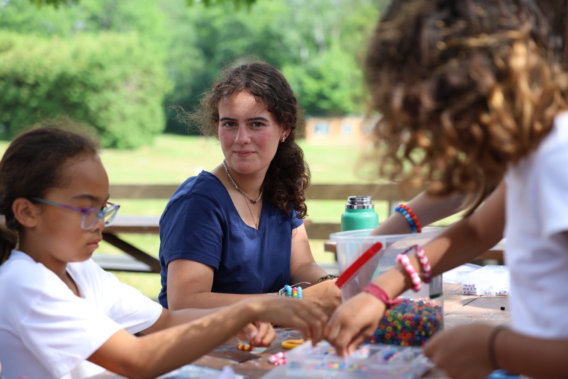 Camp Connect USA - Two children and a counsellor at a picnic table, doing arts and crafts.